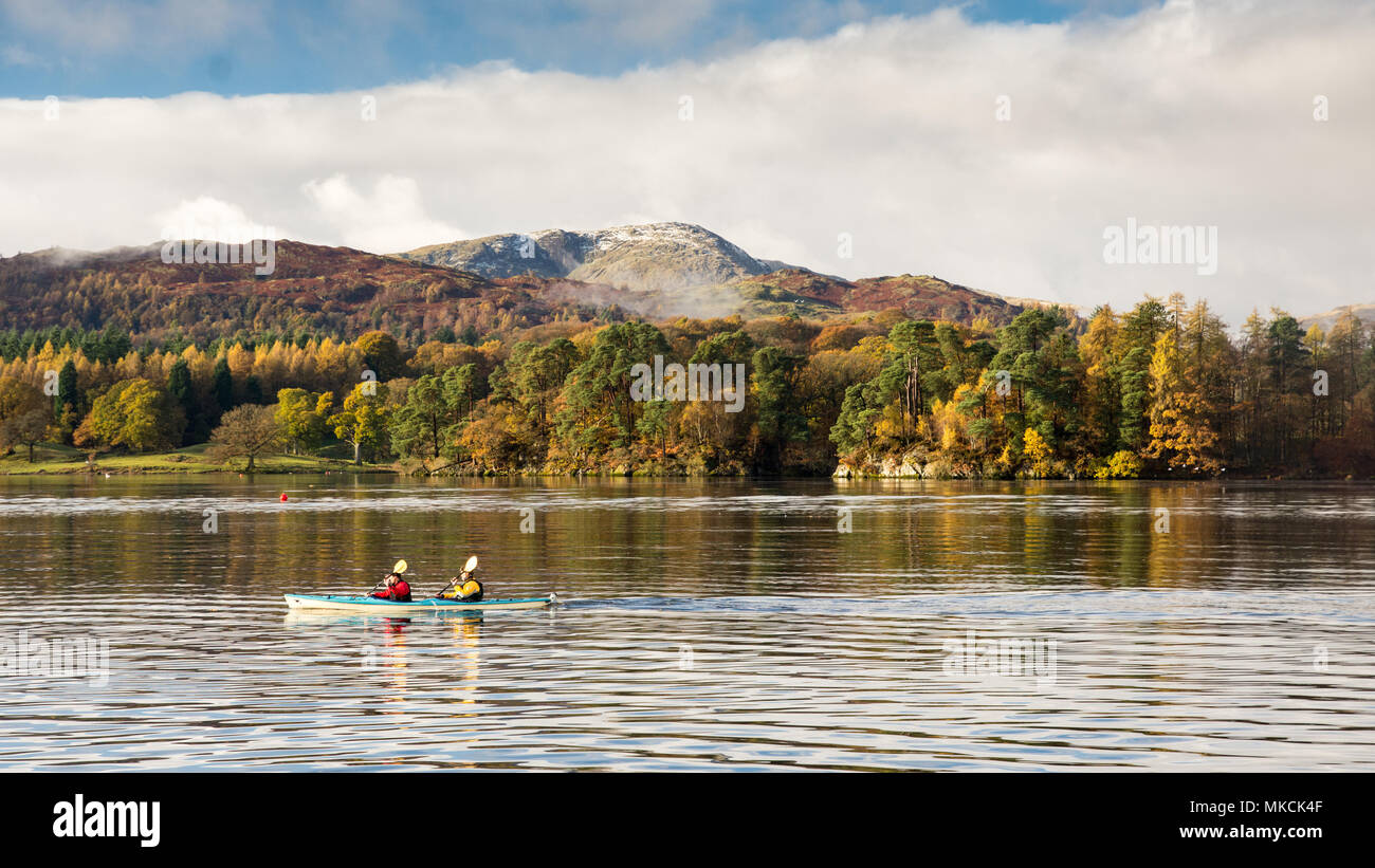 Due persone pagaiare in canoa nel lago di Windermere a Ambleside, sotto le montagne di Langdale e Bosco in autunno in Inghilterra del Lake District National Par Foto Stock