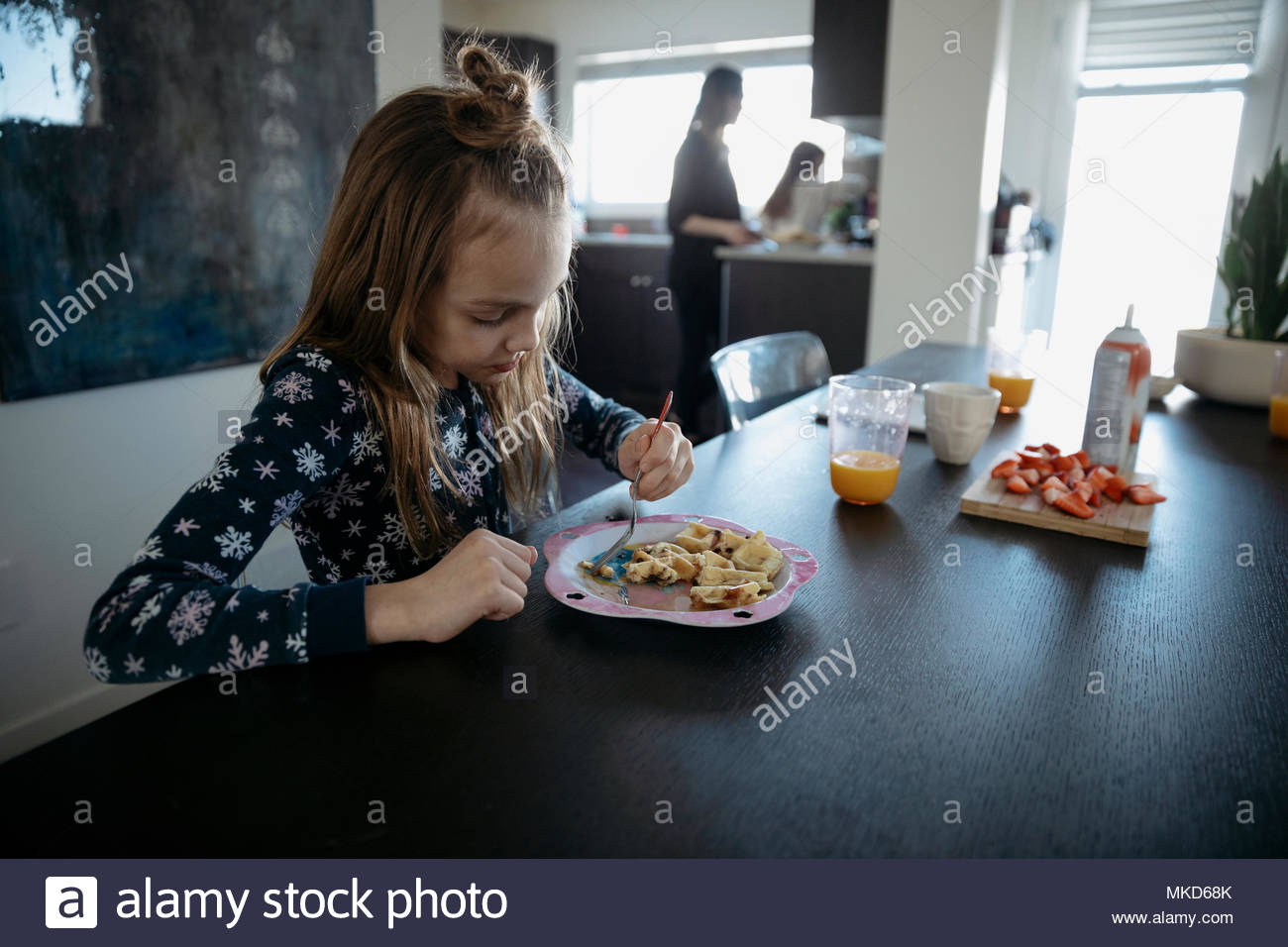 Ragazza in pigiama mangiando waffle al tavolo da pranzo Foto Stock