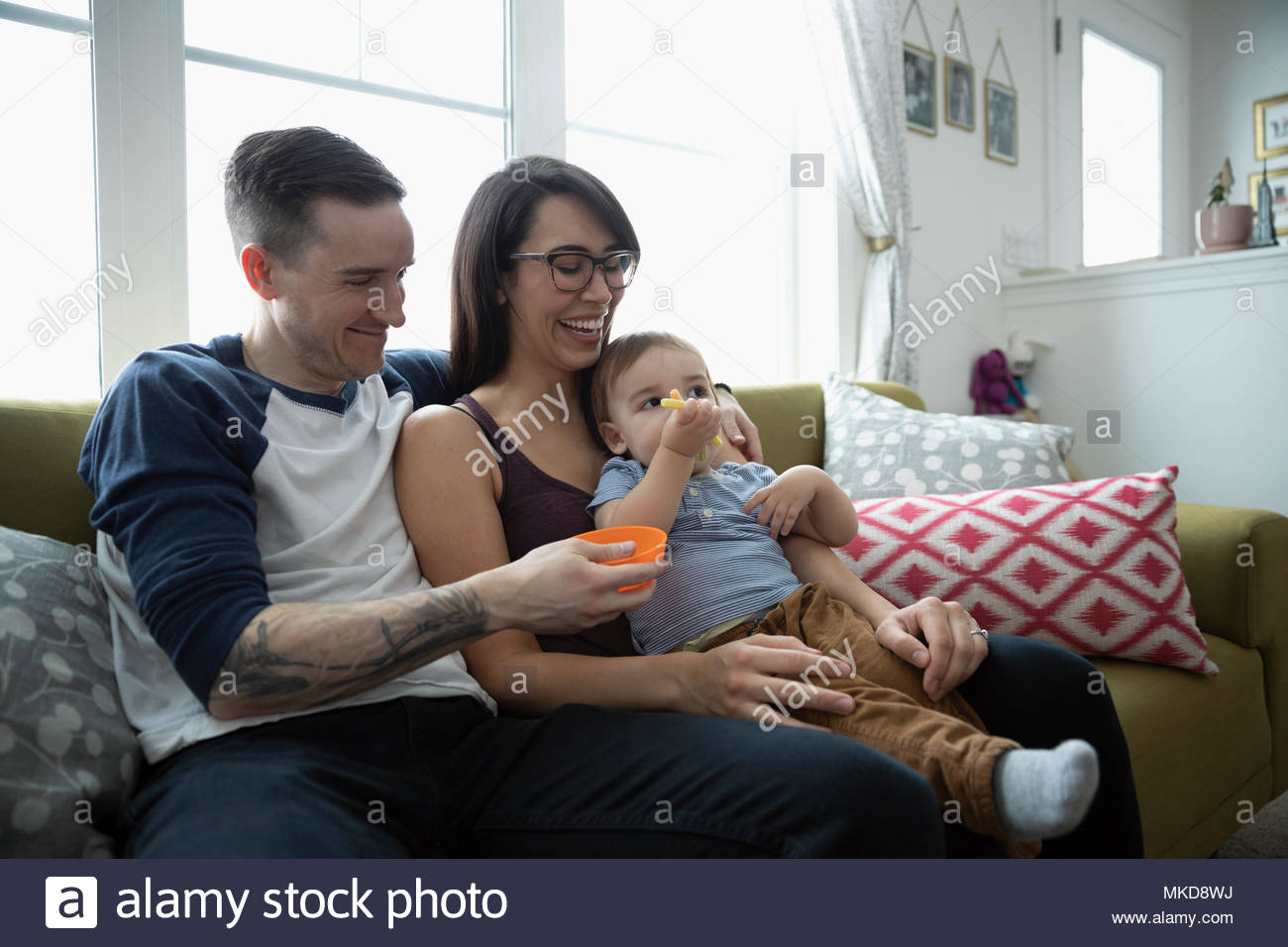 Sorridente genitori alimentazione figlio bambino sul divano Foto Stock