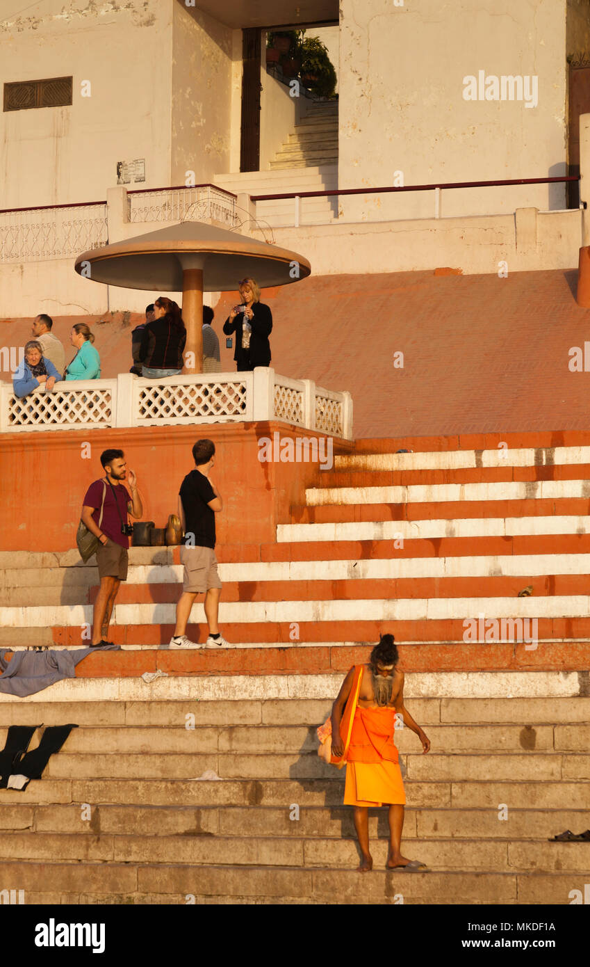 Il santo uomo in fondo agli scalini sembra essere l'intruso tra i turisti stranieri in Varanasi. Foto Stock