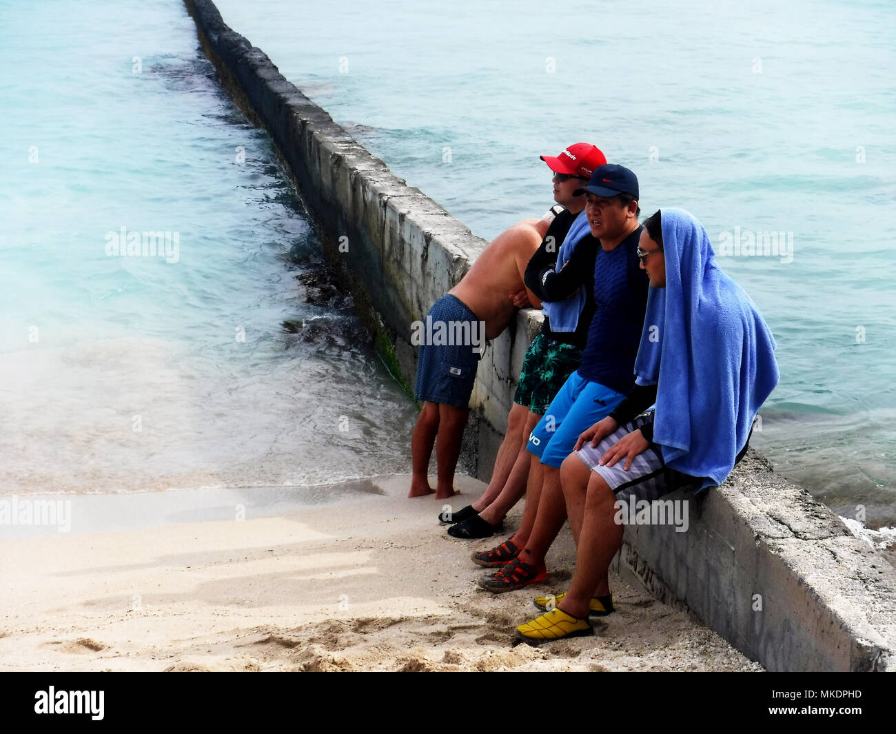 Gli uomini seduti su ocean rompe il muro presso la spiaggia di Waikiki di Oahu Hawaii Foto Stock