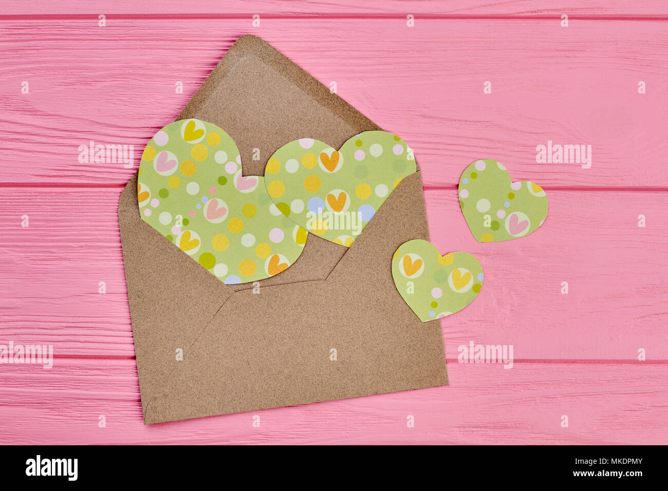 Busta da imbarcazioni carta con cuori di carta. Fatte a mano carta verde Cuori rosa su sfondo di legno. Felice il giorno di San Valentino. Foto Stock