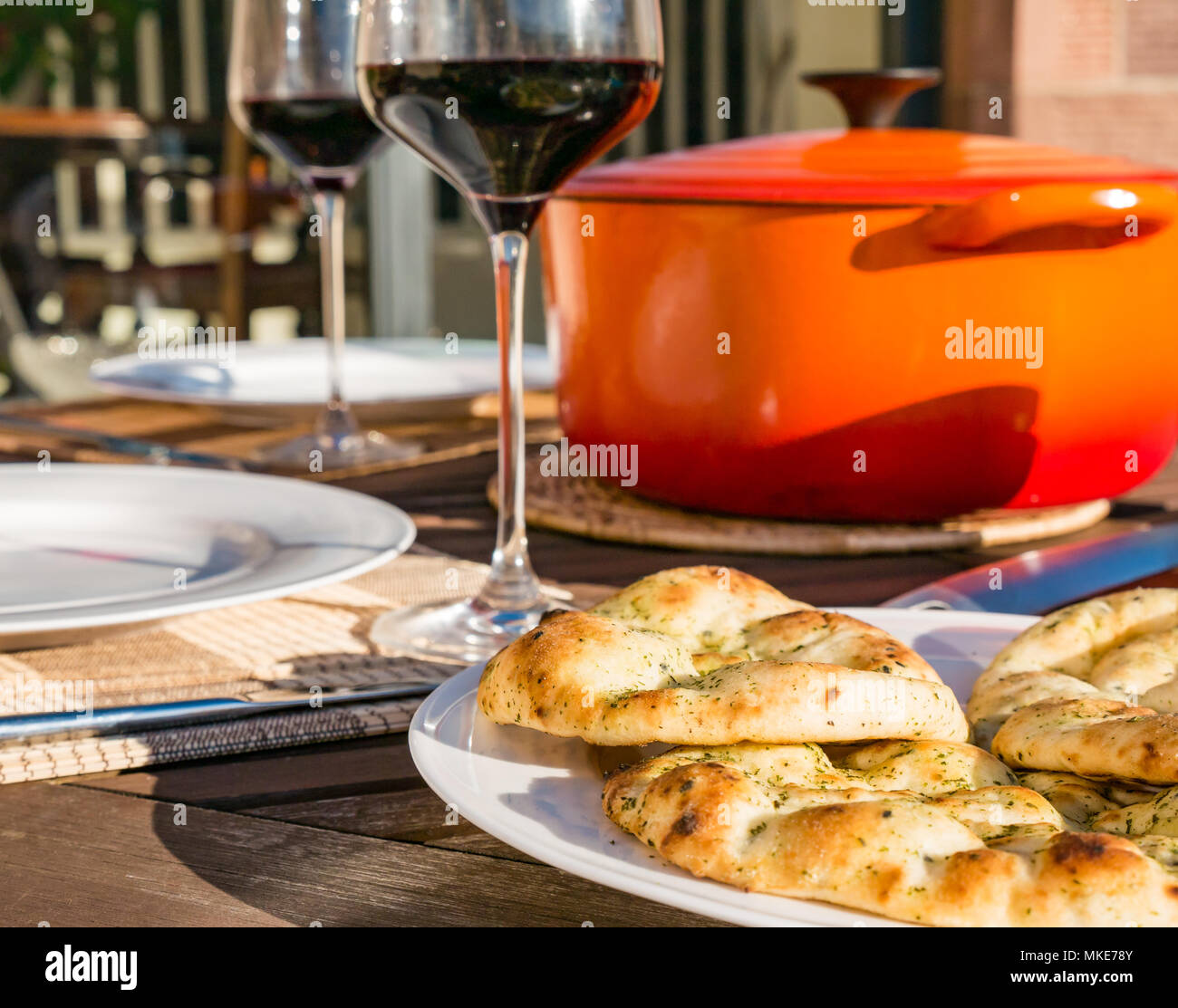 Tavolo esterno impostato con vino rosso in bicchieri e arancio Le Creuset casseruola pentola woith pane naan sulla serata di sole, Scotland, Regno Unito Foto Stock