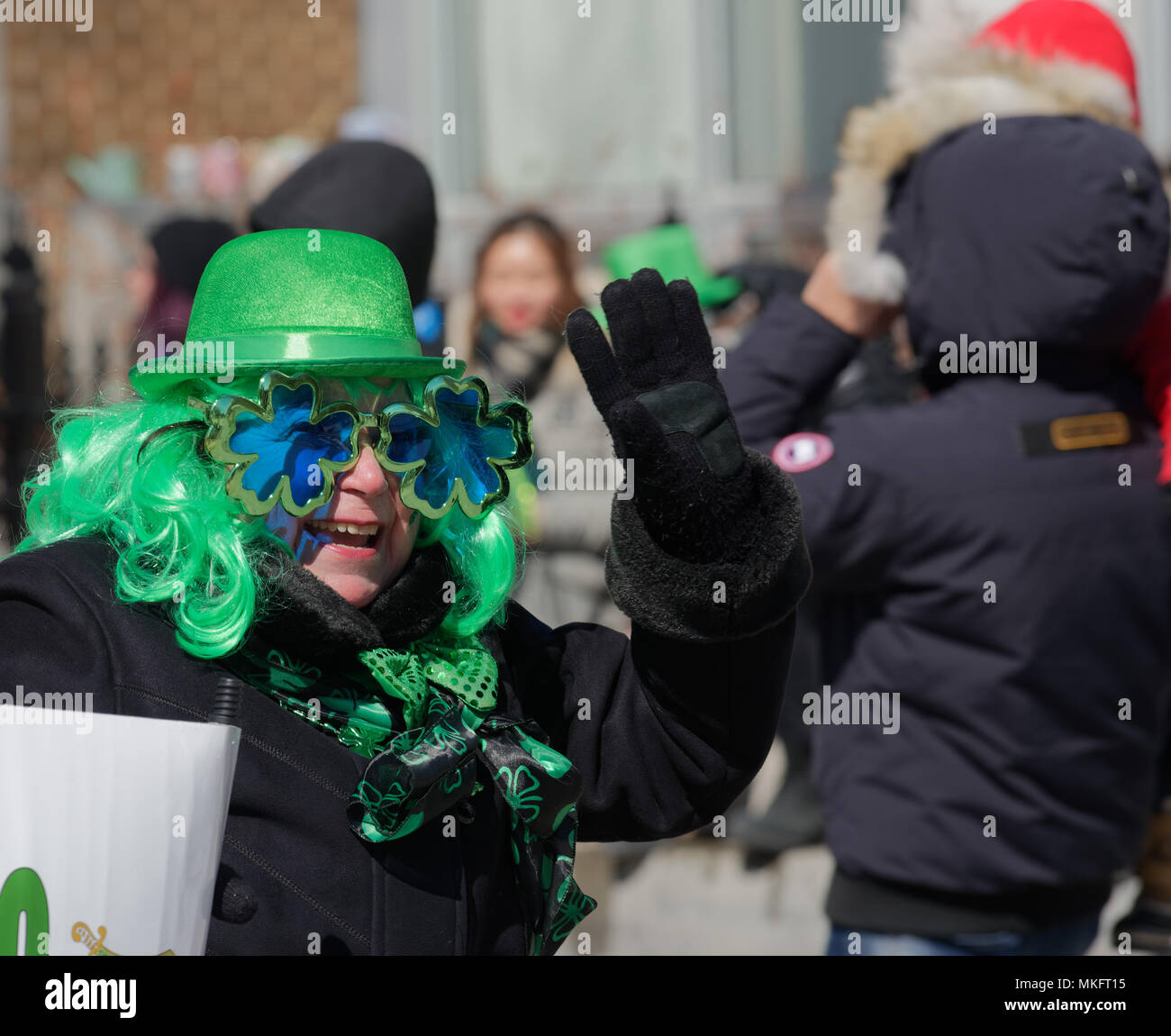 Un sorridente donna anziana indossando cappello verde e sagomato shmrock occhiali da sole a salutare la folla di San Patrizio parade di Montreal Foto Stock