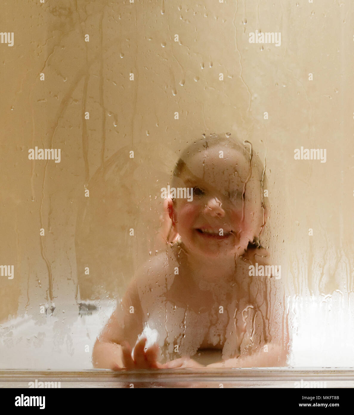 Una bambina di 3 anni di età) guardando attraverso la finestra steamy di una doccia Foto Stock