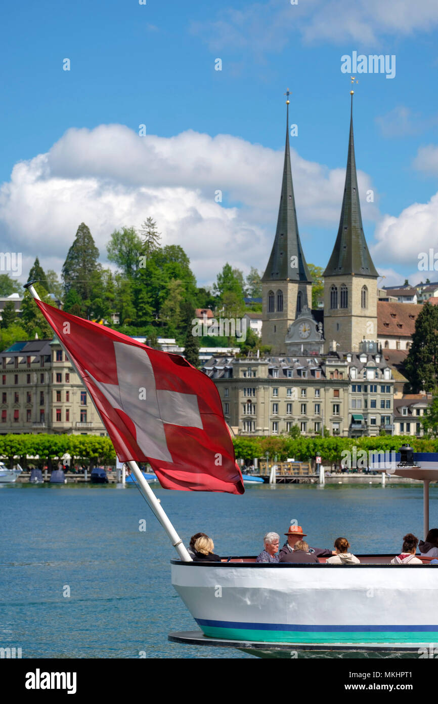 La barca con bandiera svizzera naviga sul lago di Lucerna di fronte alla Chiesa di San Leodegar, Lucerna, Svizzera, Europa Foto Stock