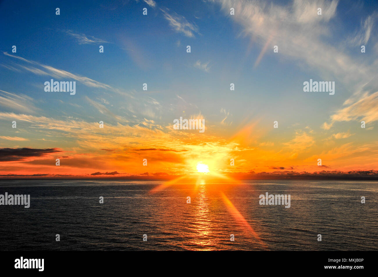 A mezzanotte il Capo Nord, Finnmark county, Norvegia. Infuocato sole tocca le montagne distanti riflettendo sopra il calmo mare di Barents Foto Stock