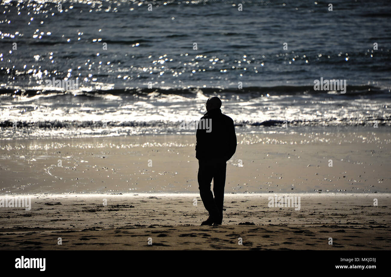 Un uomo sta guardando le onde rompono lungo il litorale, mentre il sole tramonta su un bellissimo paesaggio argenteo. Scena di spiaggia, vicino la silhouette della persona Foto Stock