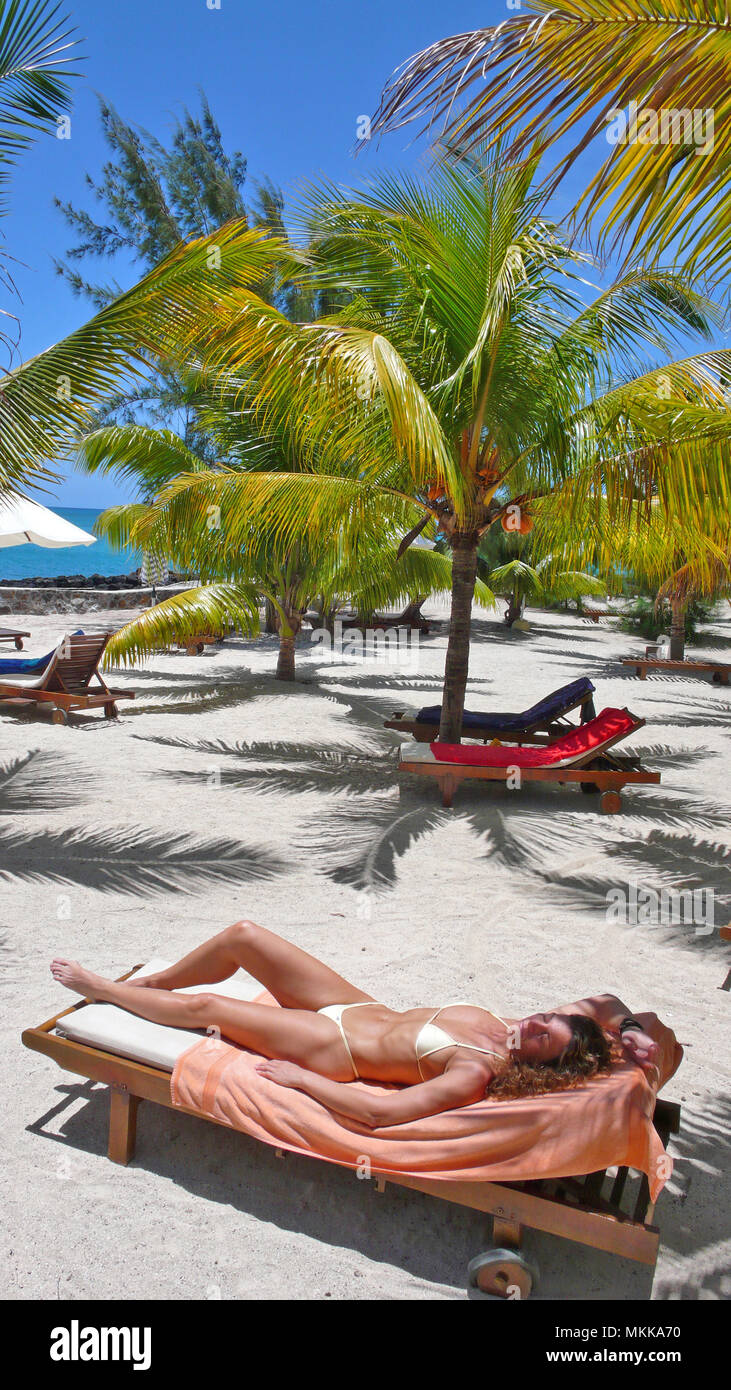 Junge Frau sonnt sich unter Offenburg am Meer | giovane donna a prendere il sole sotto palme su un lettino in una spiaggia di sabbia Foto Stock
