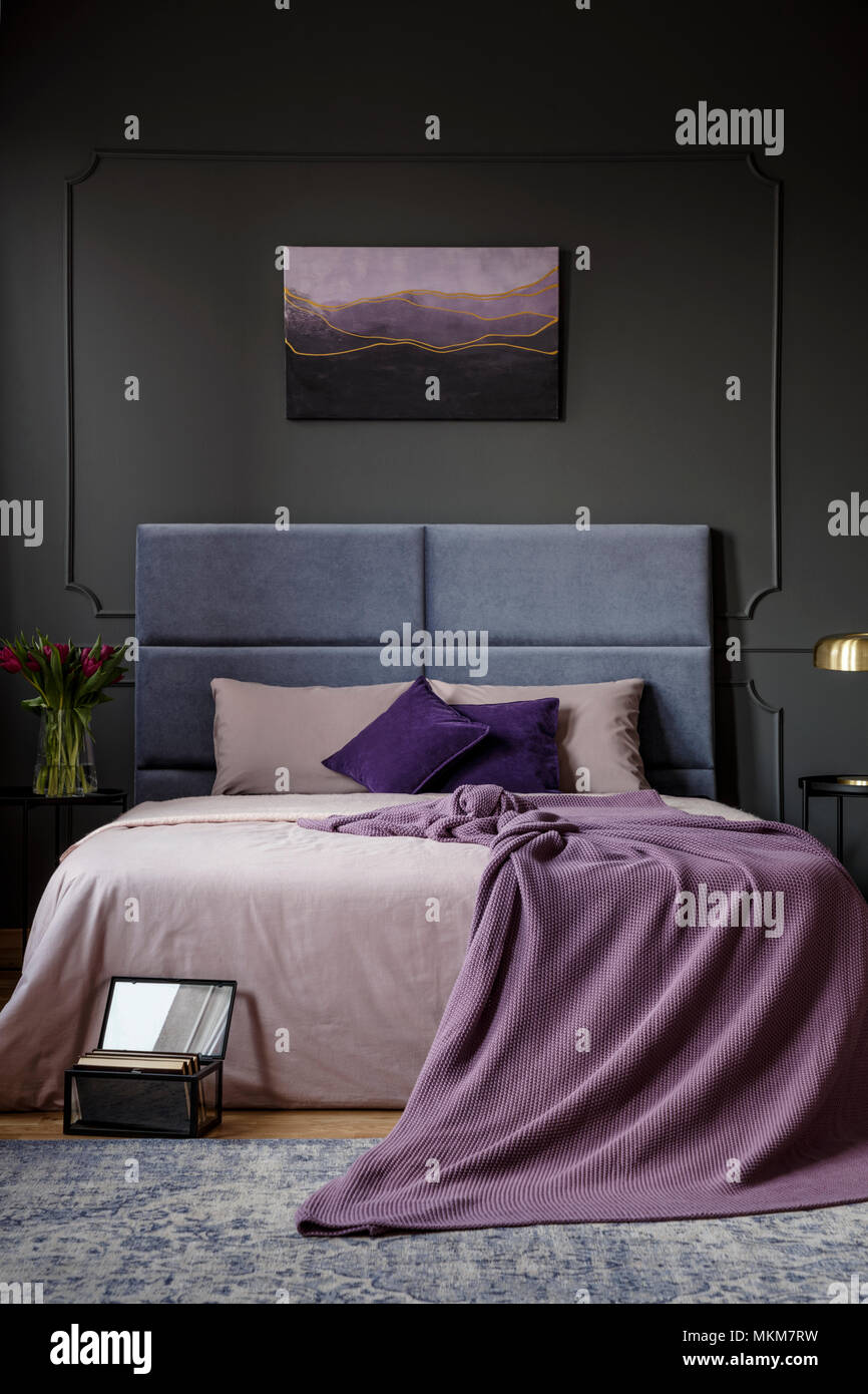 Viola coperta del letto nel buio interiore camera da letto con un dipinto sul muro grigio Foto Stock