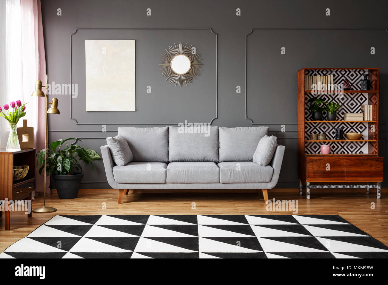 Bianco e nero Tappeto con motivo geometrico posto sul pavimento in dark living room interior con lettino grigio, vintage credenza con libri e wainsc Foto Stock