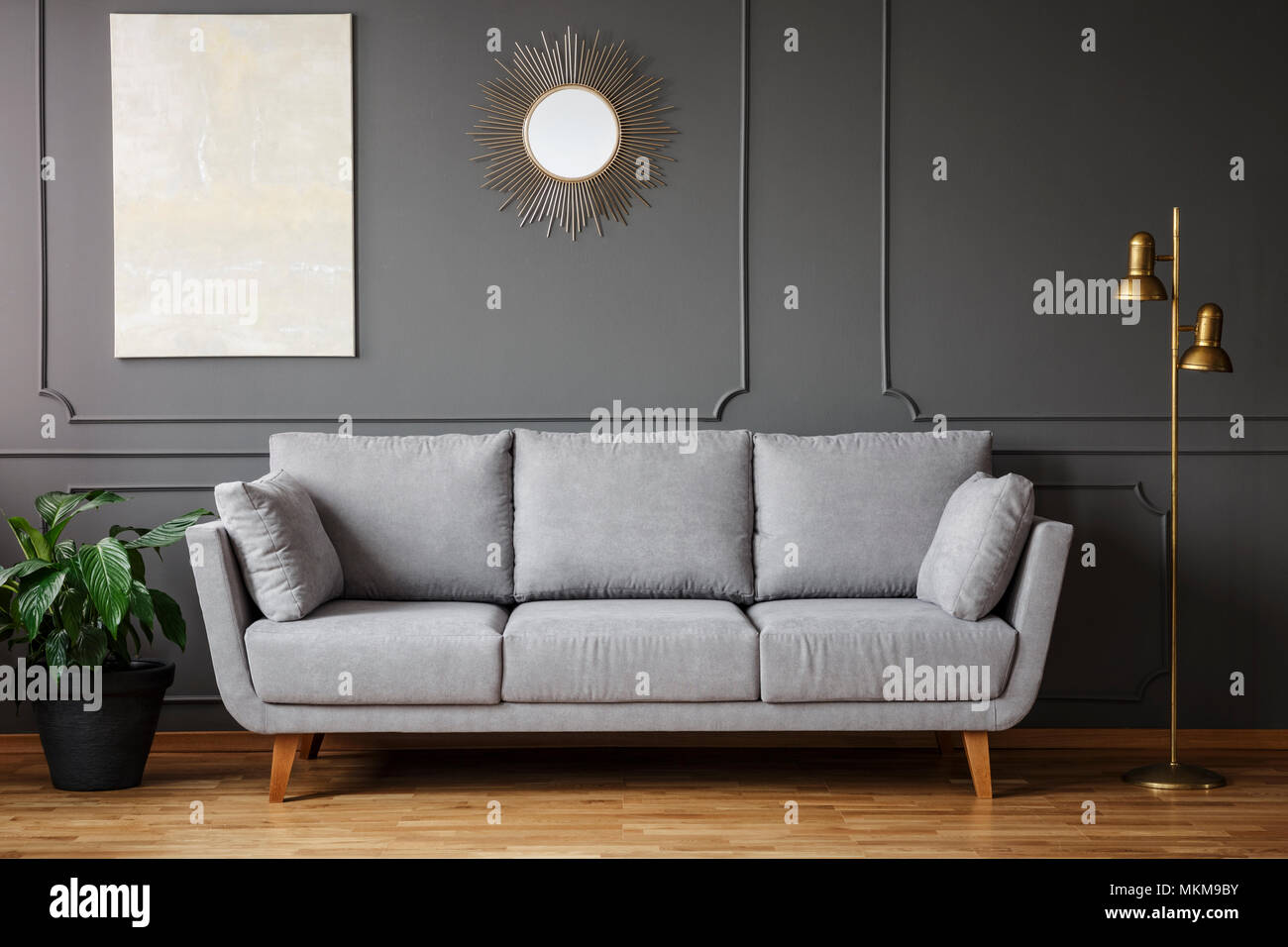 Uno specchio decorativo e pittura moderna appesi al muro con lo stampaggio in grigio scuro soggiorno interno con pianta fresca, oro lampada luminosa e divano Foto Stock