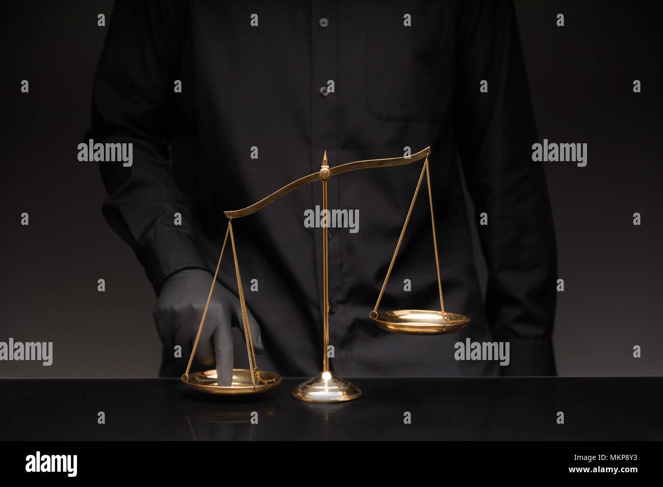 Uomo che indossa la maglia nera premendo lo squilibrio scala in vetro nero e desktop sfondo nero, imbroglio di un avvocato di ufficio, concetto di ingiustizia Foto Stock