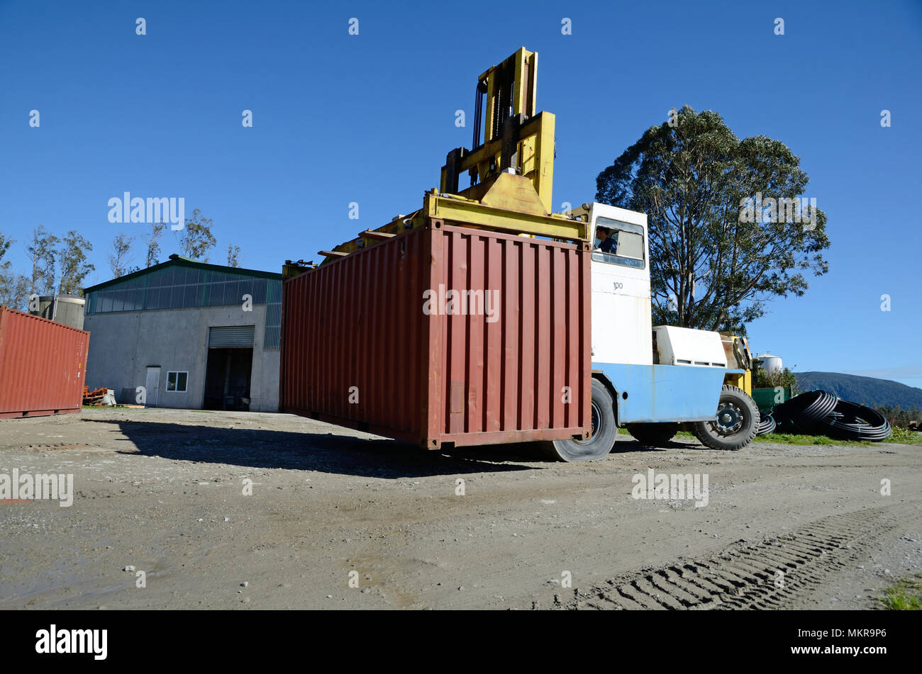 Un enorme carrello elevatore si sposta a 20 piedi di contenitore di spedizione nel cortile di una fabbrica di grandi dimensioni. Foto Stock