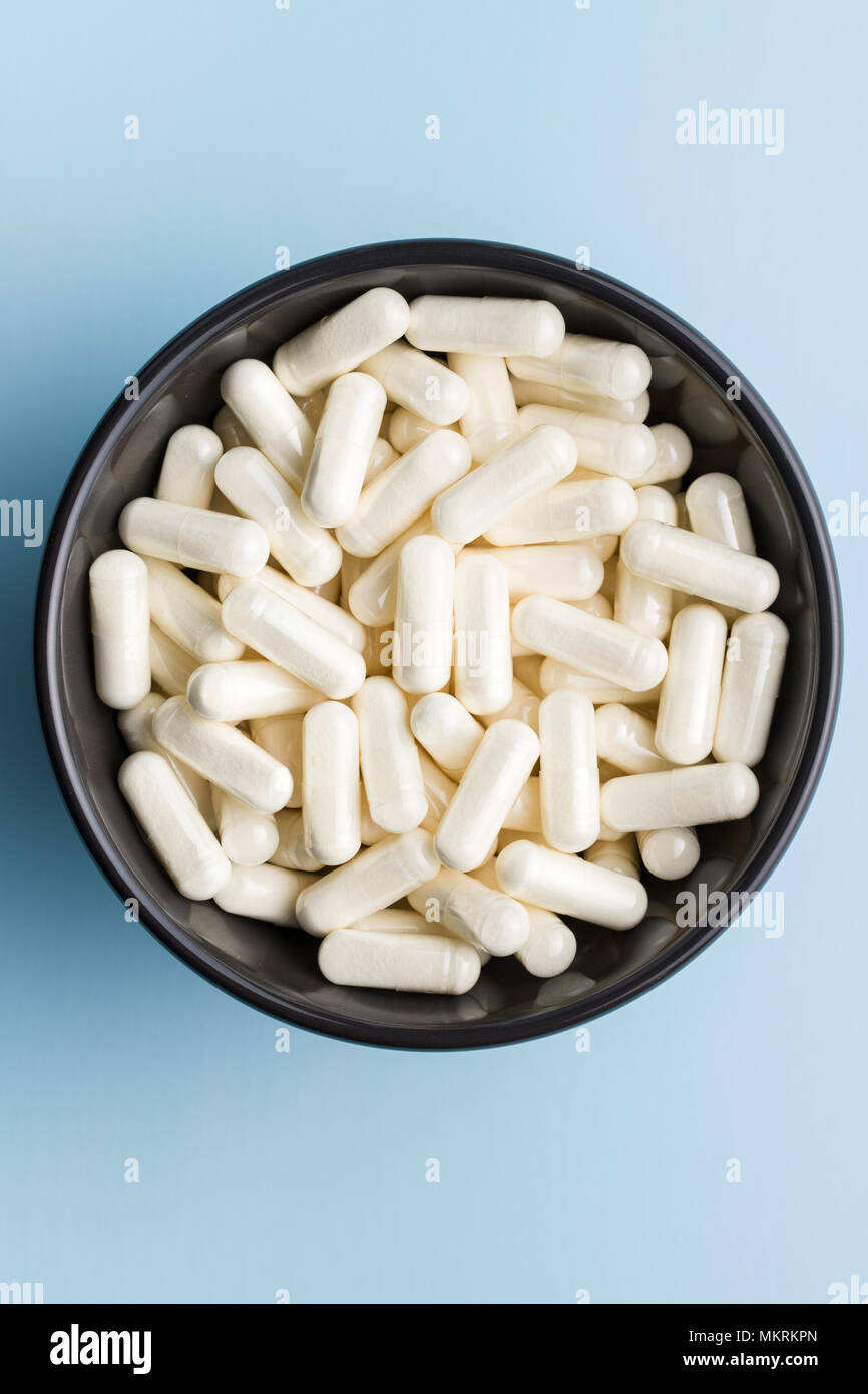 Medicina bianco capsule in ciotola su sfondo blu. Foto Stock