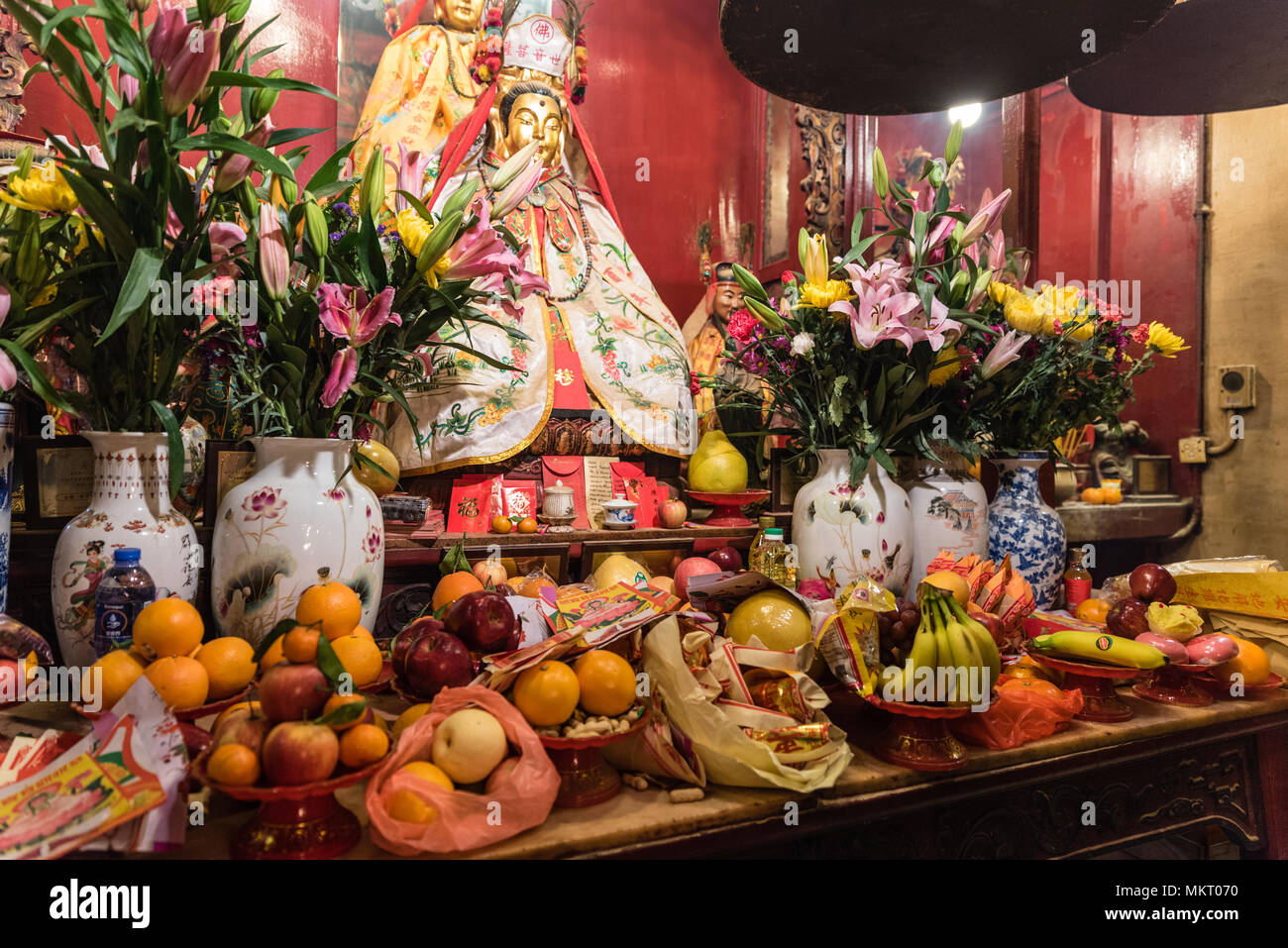 Offerte di frutti e fiori in vasi cinesi e statua dorata di Dio nel famoso tempio Man Mo, Sheung Wan, Hong Kong Foto Stock