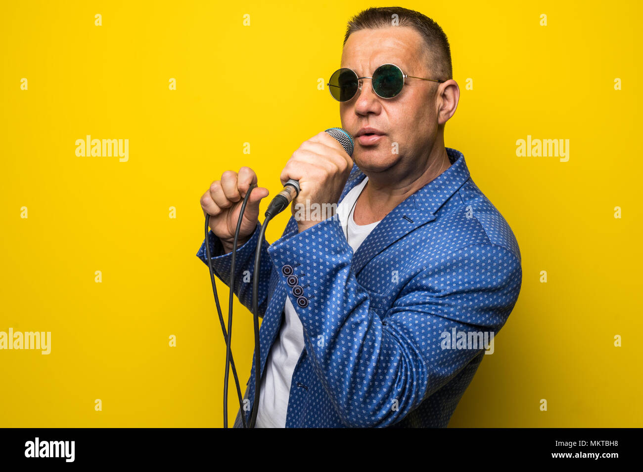 Portrai di matura età media uomo in tuta canti sul microfono isolato su sfondo giallo. Foto Stock