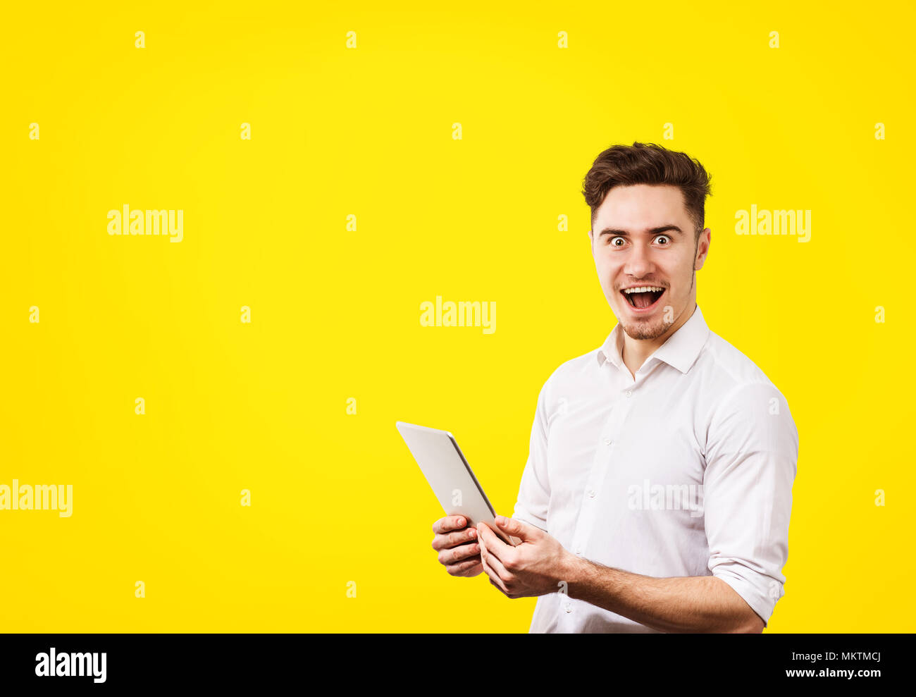 Sorpreso giovane uomo che indossa una camicia bianca con tablet pc isolati su vivid sfondo giallo Foto Stock