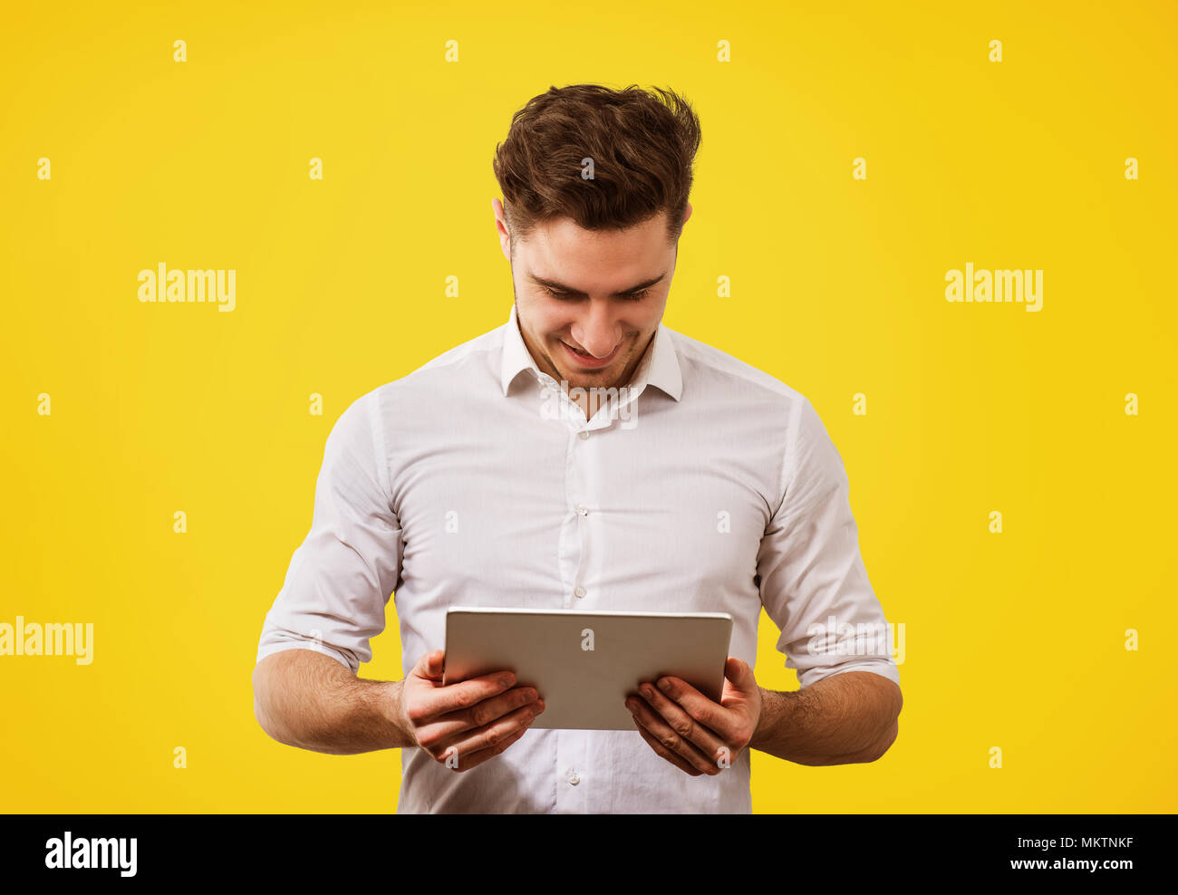 Giovane uomo bello in maglia bianca cercando felice mentre navighi in Internet nuovo tablet su sfondo giallo. Foto Stock