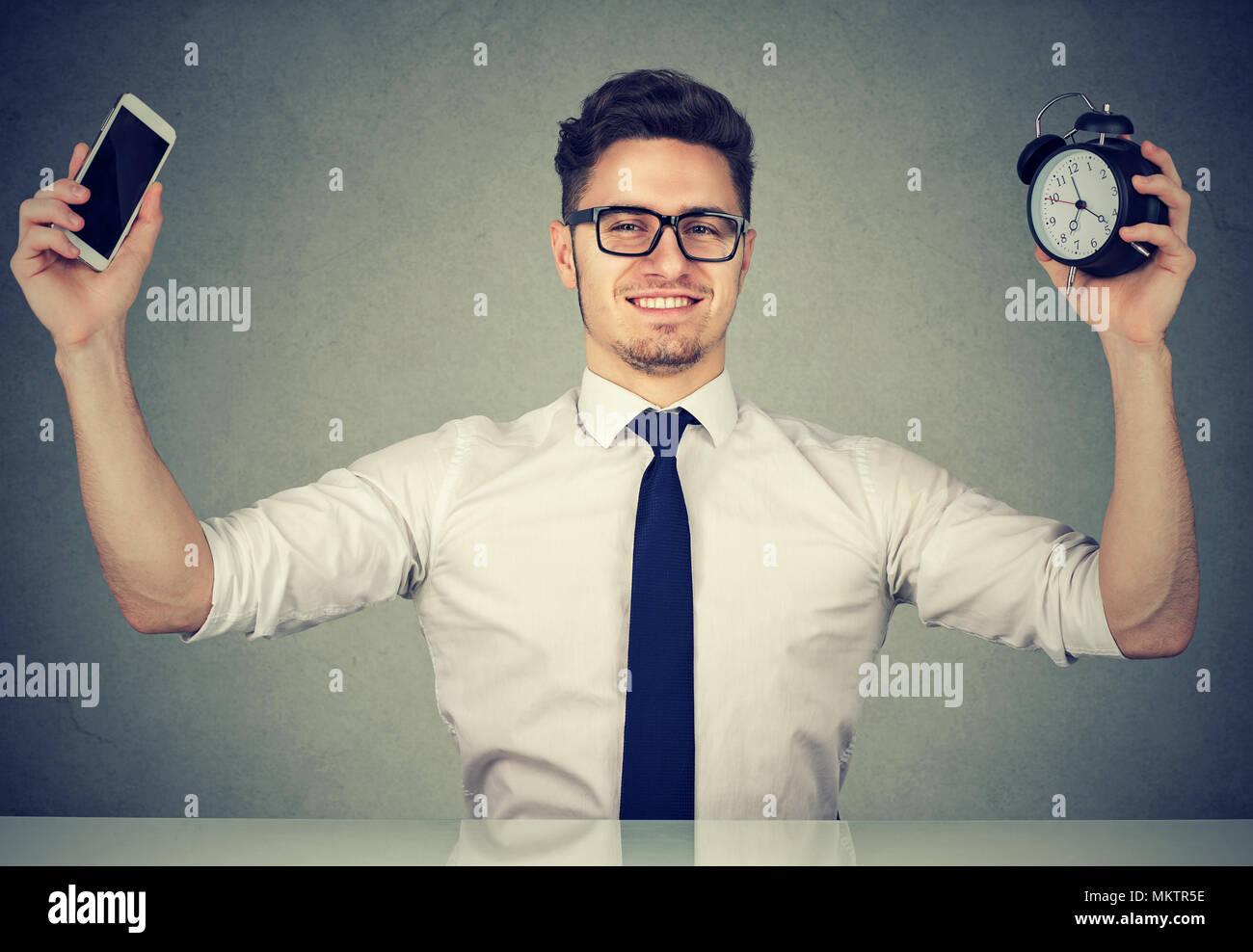 Contenuto di giovane lavoratore titolare smartphone e sveglia di trascorrere del tempo con gadget al lavoro. Foto Stock