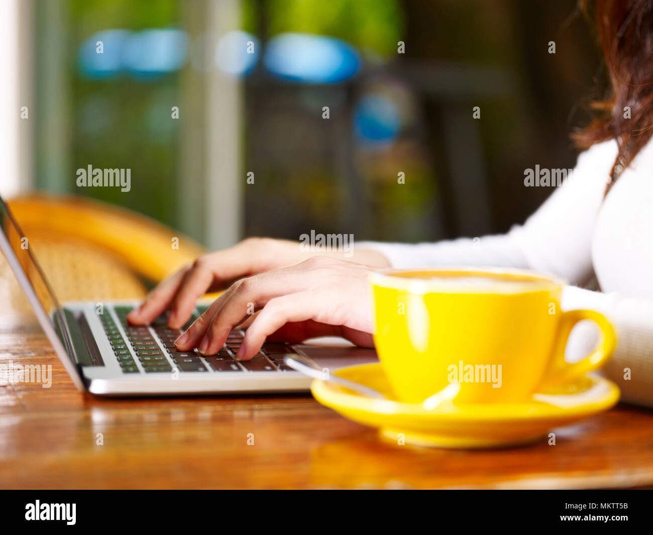 Giovane donna asiatica utilizzando computer portatile mentre si beve il caffè. Foto Stock