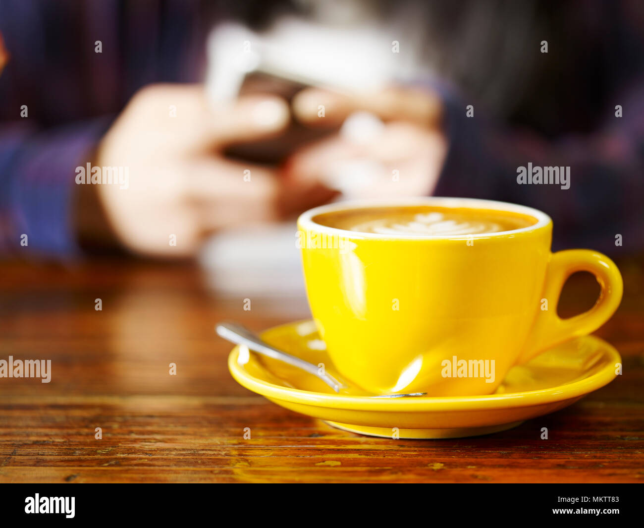 Donna che gioca con il telefono cellulare mentre si beve il caffè cappuccino, concentrarsi sulla coppa. Foto Stock