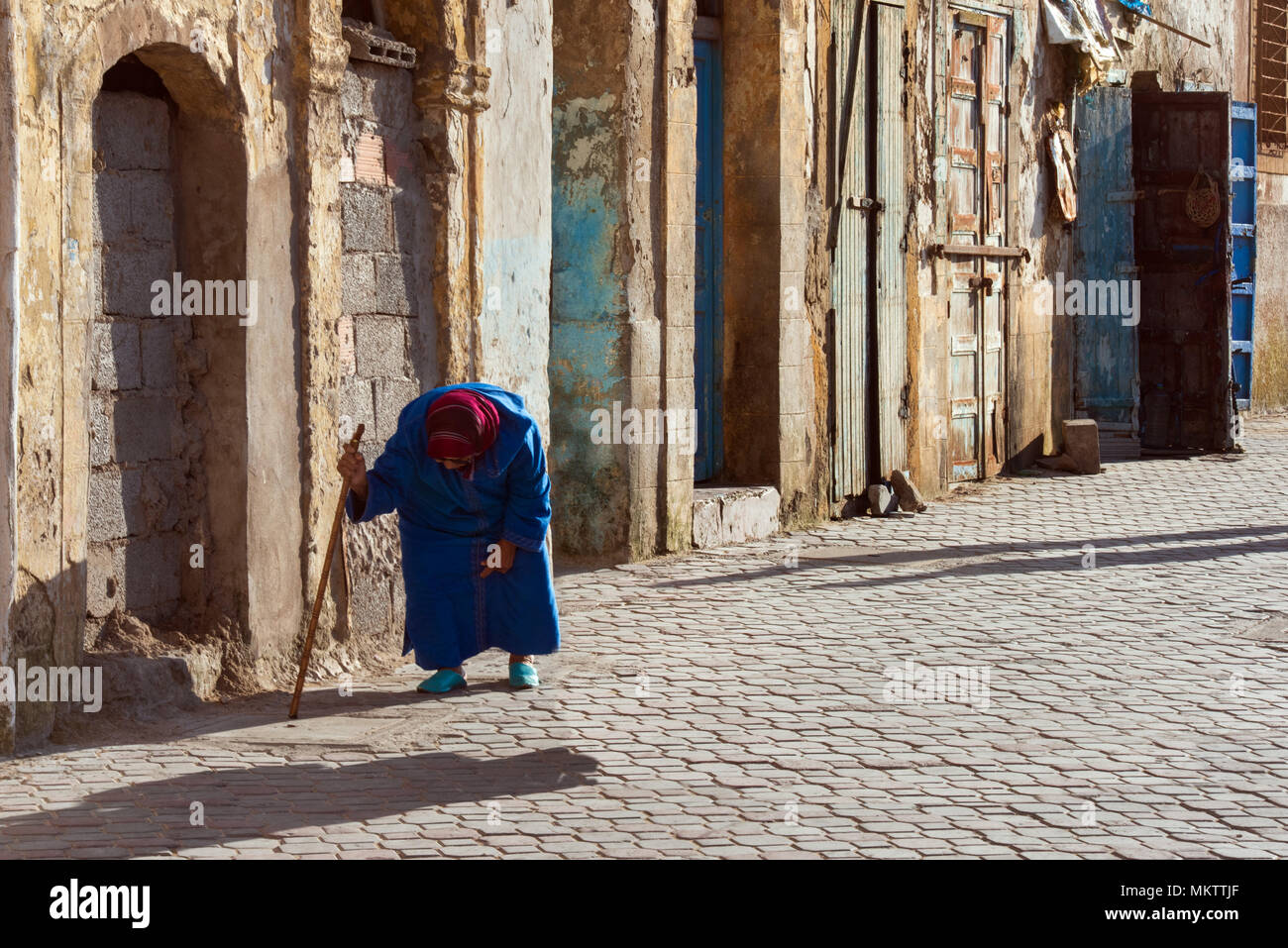 Odf piegate donna cammina con una bacchetta lungo le antiche mura della medina di Essaouira, Marocco. Foto Stock