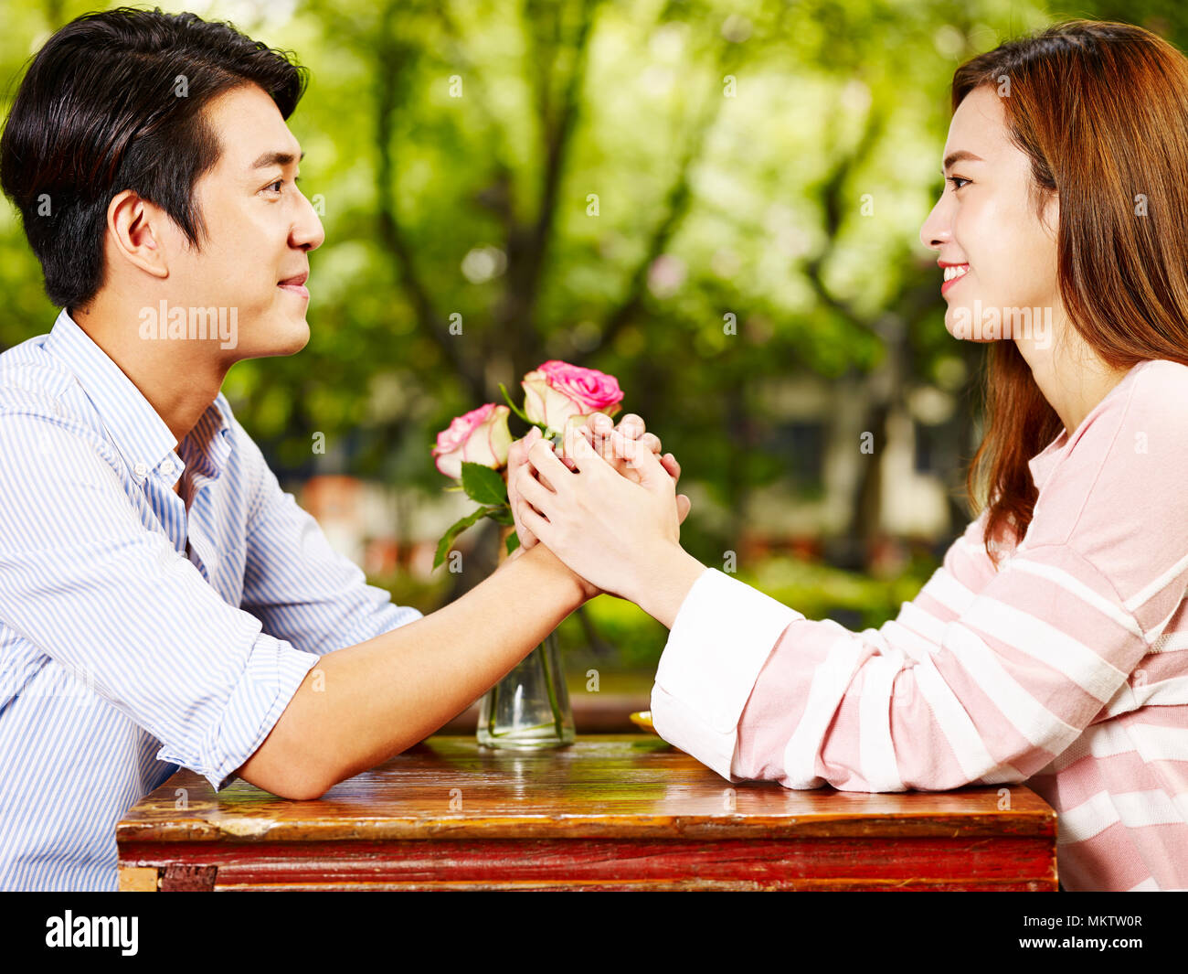 Giovani asiatici l uomo e la donna seduta faccia a faccia tenendo le mani guardando ogni altro nella caffetteria. Foto Stock