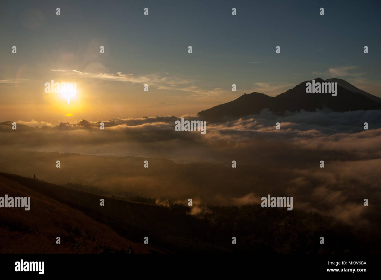 Come sole di mattina sorge sopra l'orizzonte, la luce si diffonde attraverso basse nubi sul Lago Batur. Nelle vicinanze, Monte Agung inizia a rivelare più texture. Foto Stock