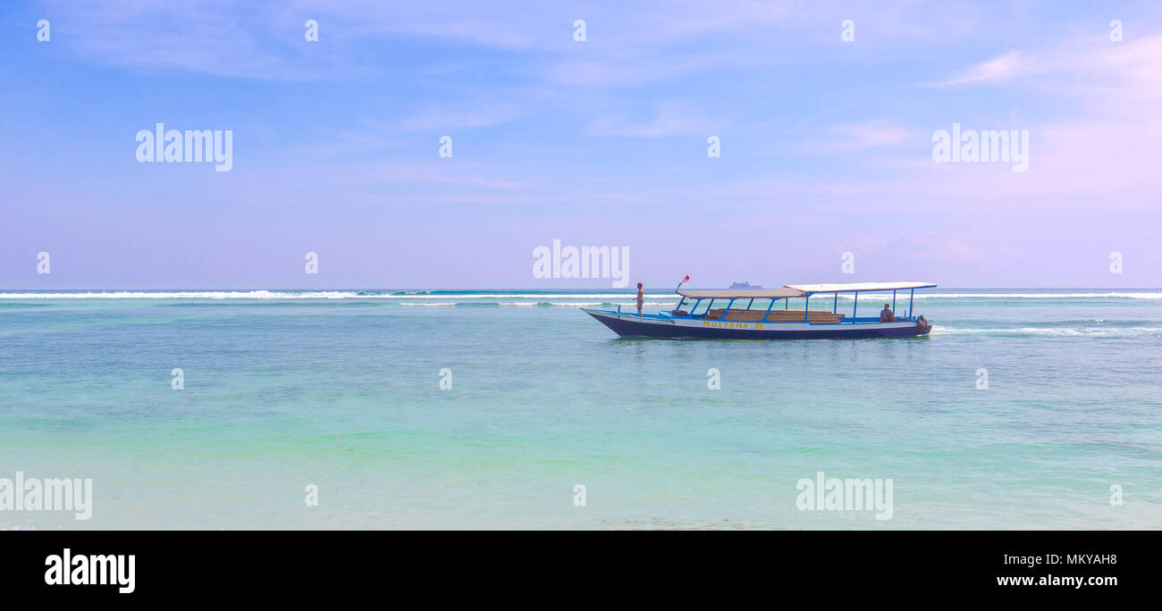 I marinai alla guida di una lunga coda imbarcazione cargo nell'oceano turkuoise, la barca è caricato con il legname e dei rotoli di onde, Gili Trawangan, Indonesia, aprile Foto Stock