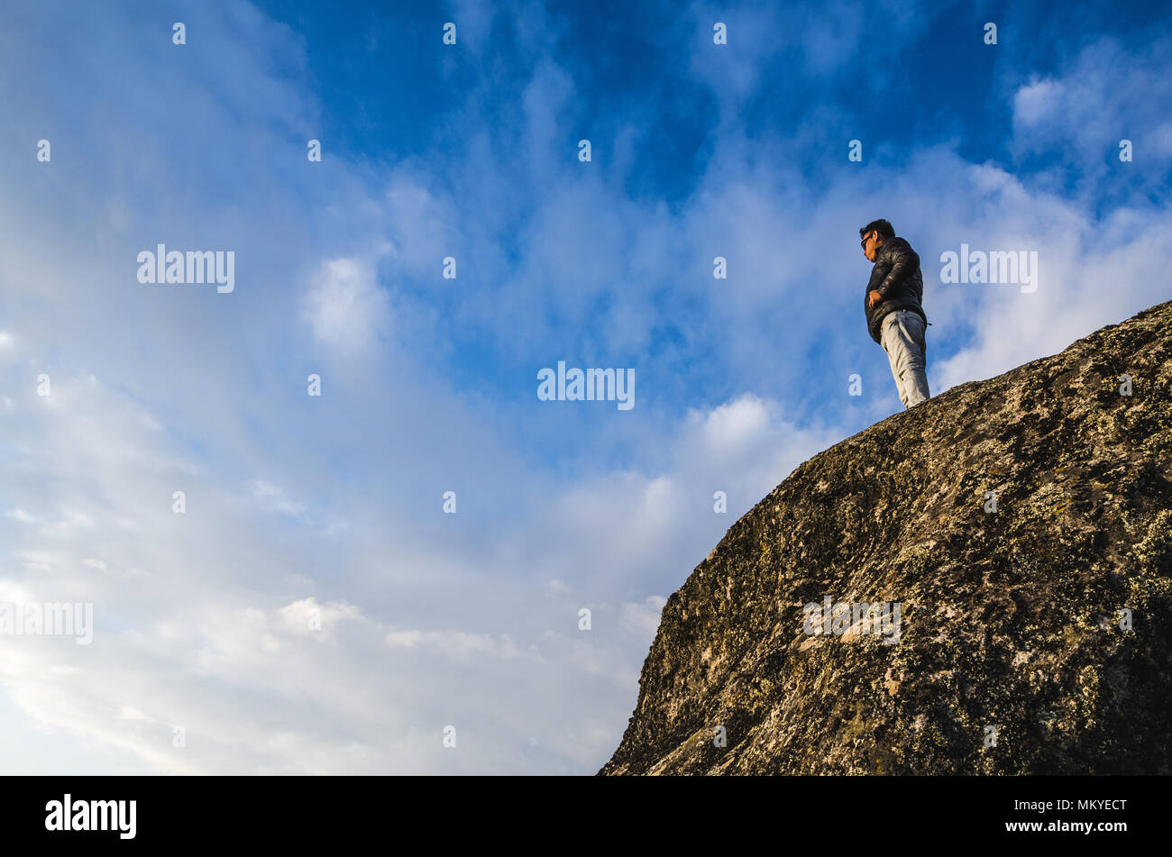 Giovane uomo ai piedi di una scogliera guardando l'orizzonte Foto Stock