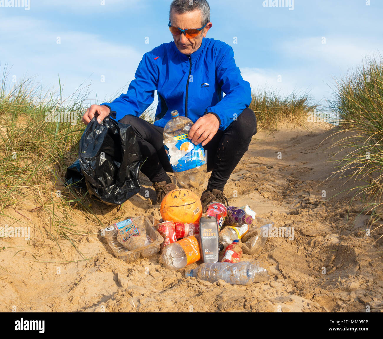 Un pareggiatore Plogging (prelievo di lettiera durante il jogging) sulla sua corsa mattutina attraverso le dune di sabbia.UK Foto Stock
