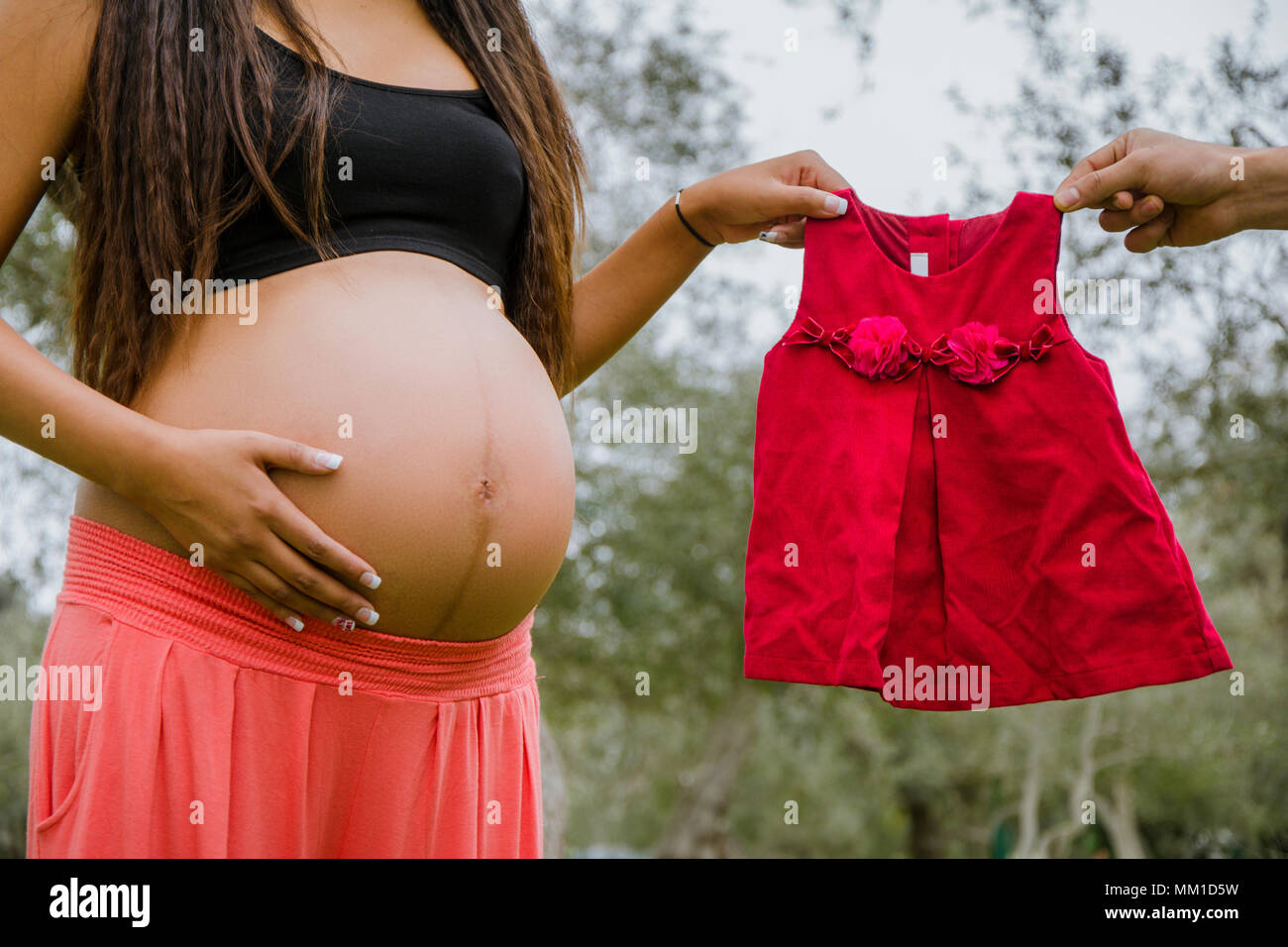 Abito rosso accanto al ventre di una donna in stato di gravidanza Foto Stock