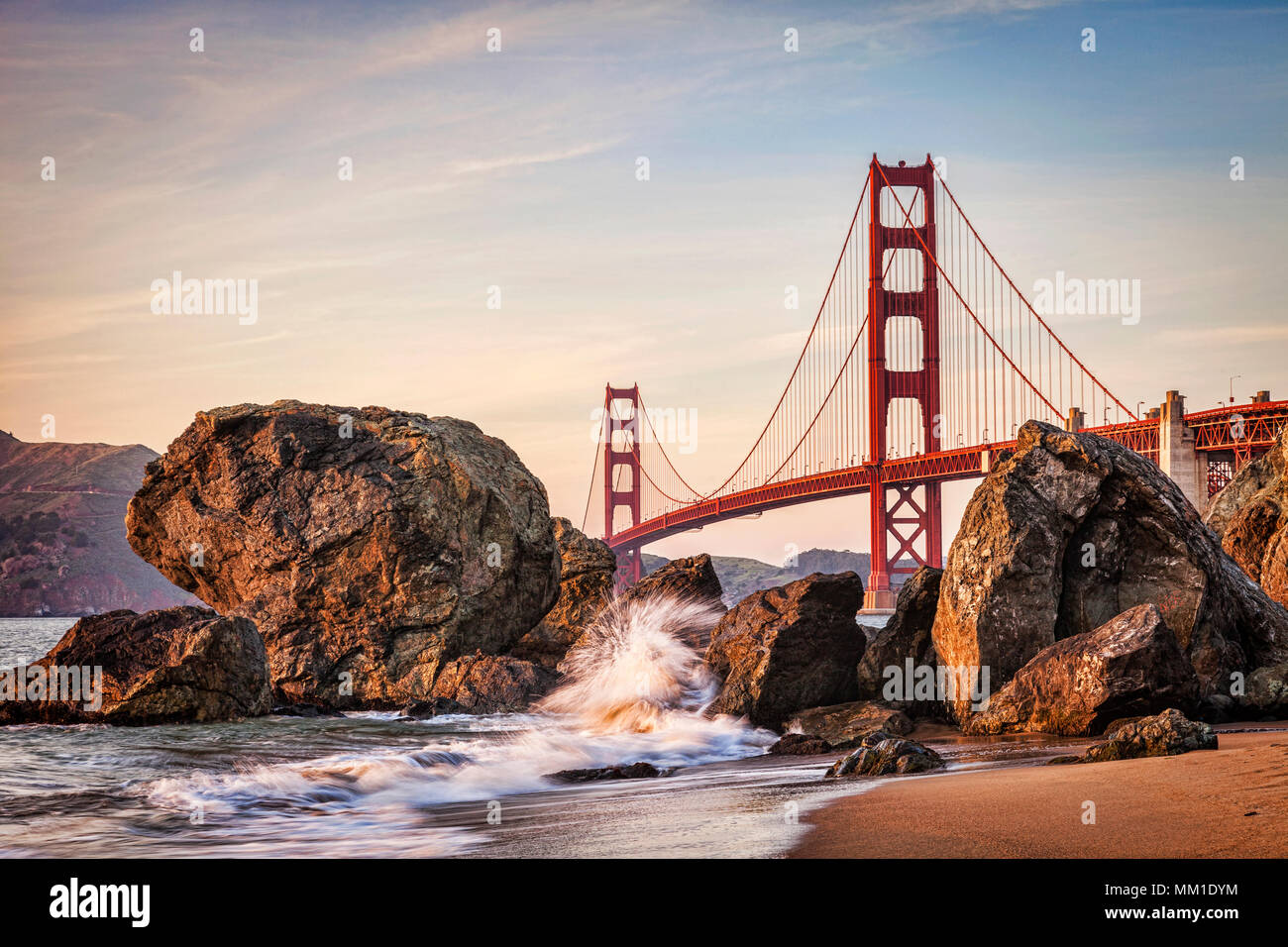 Golden Gate Bridge di San Francisco, avvicinando il tramonto., con un'onda schizzi fino contro le rocce. Foto Stock