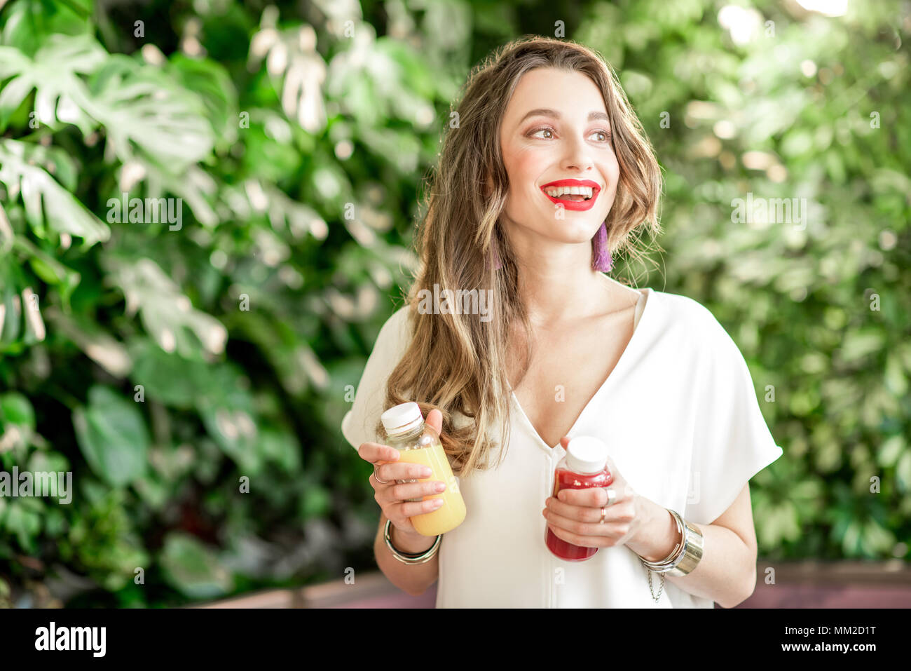 Ritratto di una giovane donna felice tenendo le bottiglie con frullato sano le bevande in piedi sullo sfondo verde Foto Stock