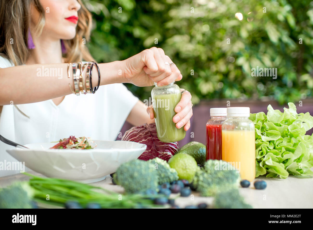 Donna di prendere una bottiglia con drink frullato dal tavolo pieno di sani ingredienti alimentari in ambienti interni Foto Stock