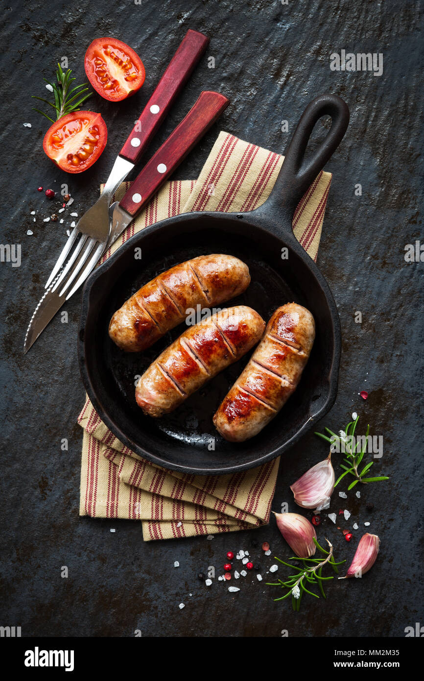 Carne di maiale alla griglia salsicce o petardi in padella in ghisa o in padella con pomodori, aglio e rosmarino. Vista aerea Foto Stock