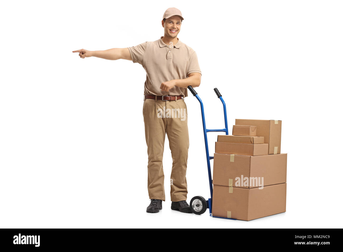 A piena lunghezza Ritratto di una consegna uomo appoggiato su di un lato carrello caricato con scatole e puntamento isolati su sfondo bianco Foto Stock