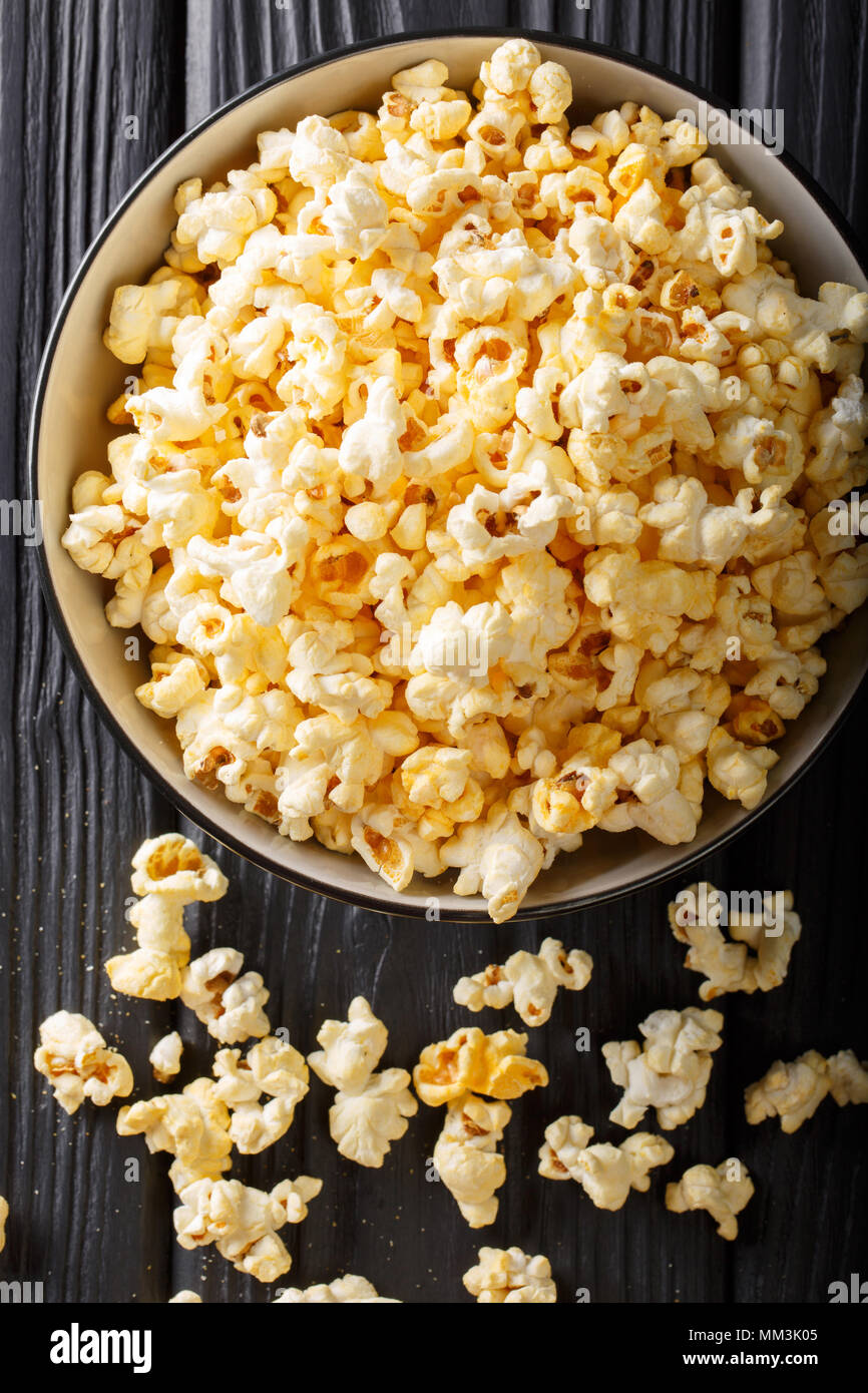 Popolari: snack salati popcorn con il formaggio Cheddar e il parmigiano in una ciotola vicino sul tavolo. Verticale in alto vista da sopra Foto Stock