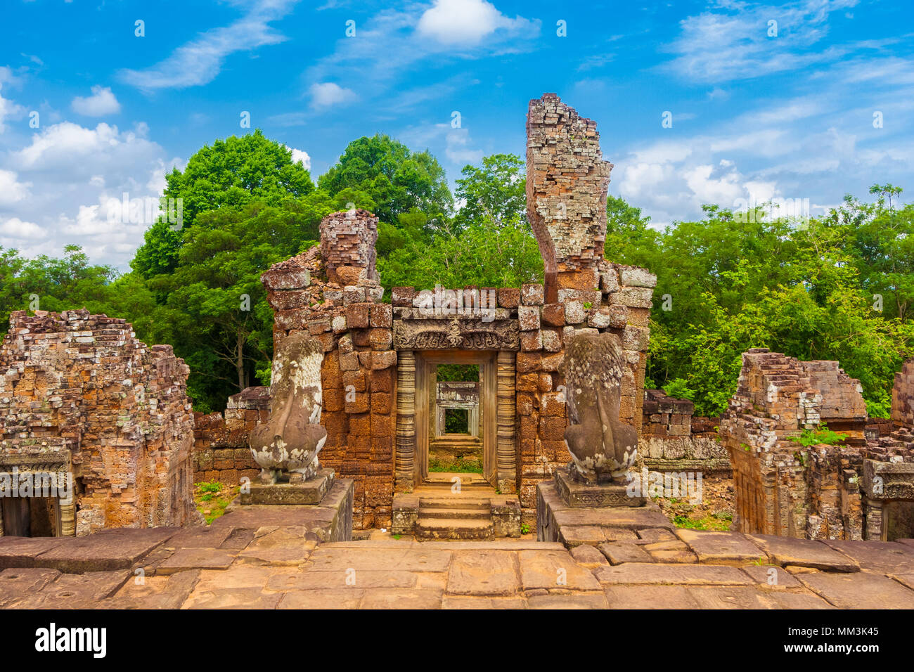 Il mattone di laterite rovina della torre sul lato ovest della terrazza centrale visto dietro il custode lion statue della Cambogia East Mebon tempio. Foto Stock