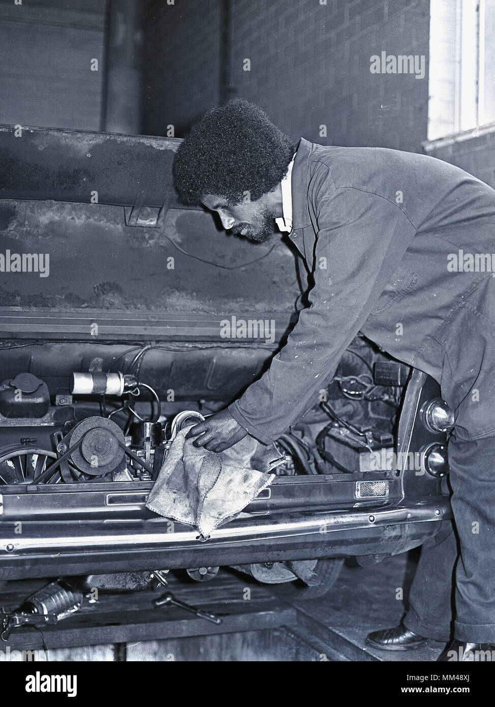 Anni Settanta, maschio adulto meccanico lavora sul motore di un veicolo a motore nel sud di Londra, Inghilterra, Regno Unito. È il motore posteriore auto, in modo che potrebbe essere una vettura a motore come un Hillman Imp. Foto Stock