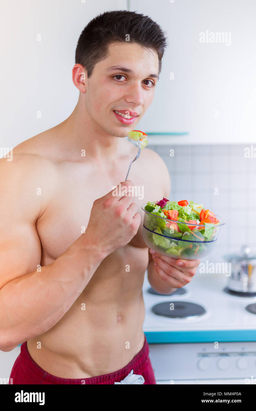 Giovane uomo mangiare insalata in cucina mangiare sano formato ritratto vegetariano vegano Foto Stock