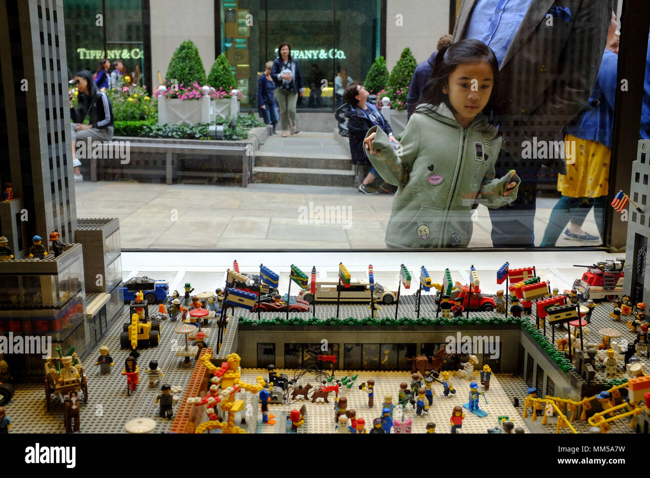 Una giovane ragazza asiatica guarda attraverso la finestra del negozio Lego in corrispondenza di un visualizzatore del Rockefeller Center di New York City il 6 maggio 2018. Foto Stock