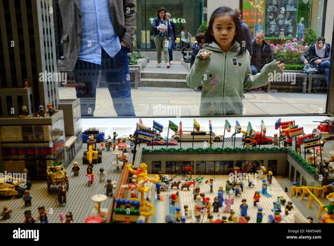 Una giovane ragazza asiatica guarda attraverso la finestra del negozio Lego in corrispondenza di un visualizzatore del Rockefeller Center di New York City il 6 maggio 2018. Foto Stock