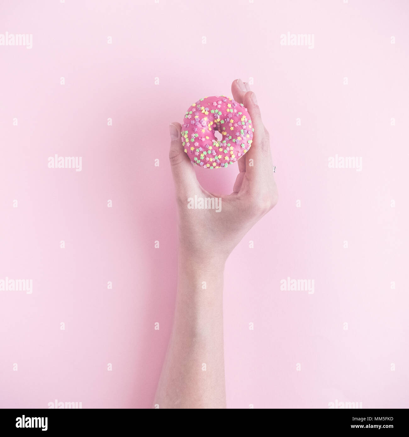 Stretta di mano femminile azienda piccola ciambella pastello su sfondo rosa minimo concetto creativo. Foto Stock