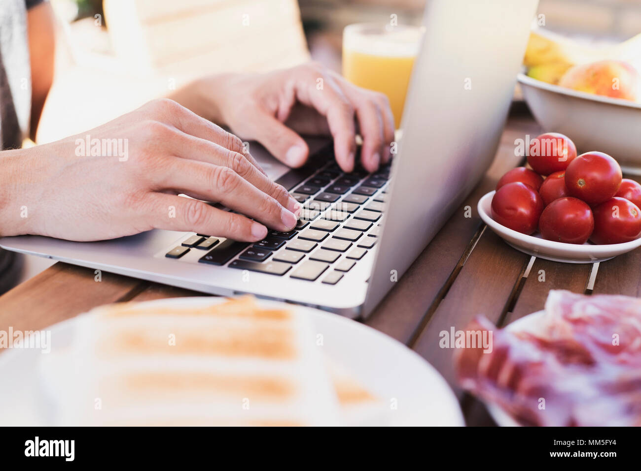 Primo piano di un giovane uomo caucasico usando un computer portatile seduti ad un tavolo di legno all'aperto durante un pasto Foto Stock