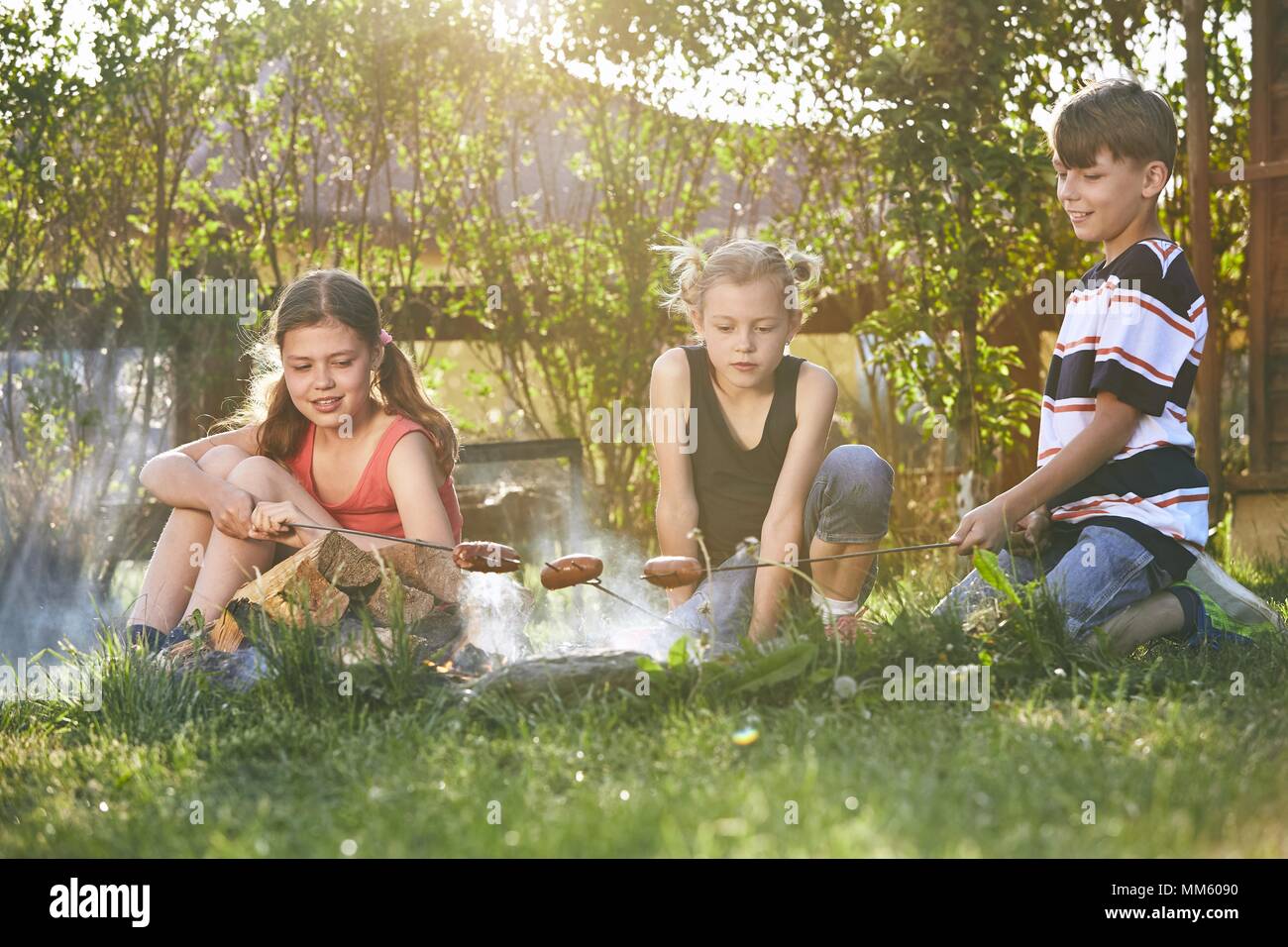 I bambini godono di falò. I fratelli (famiglia) salsicce di tostatura sul giardino al tramonto. Foto Stock