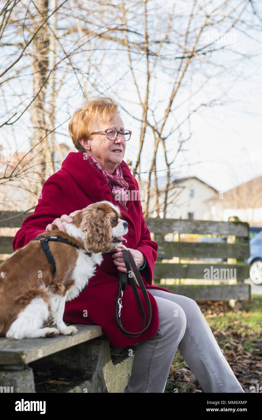 Donna anziana e il suo cane al di fuori seduta sul banco di lavoro Foto Stock