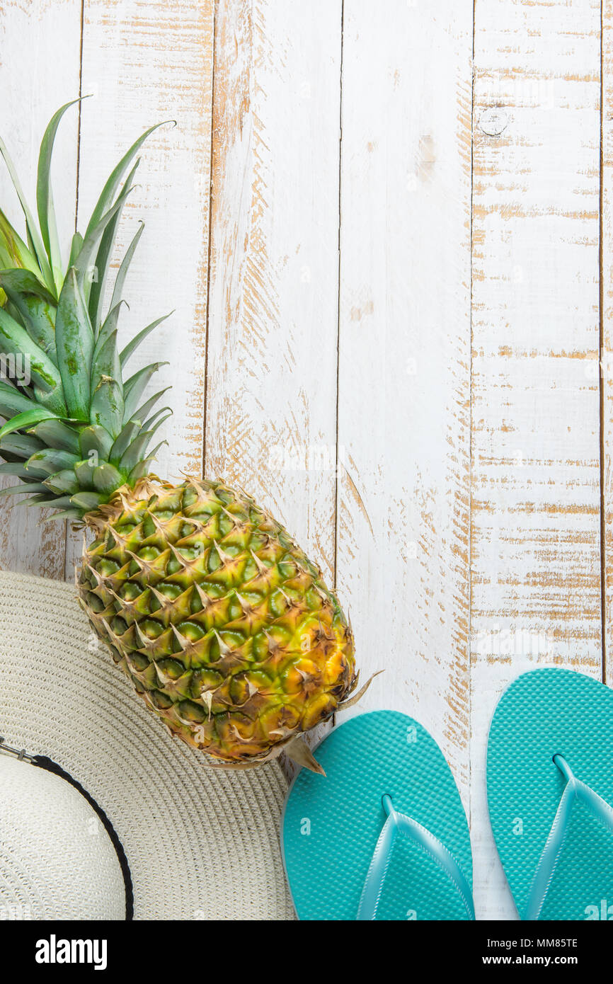 Piatto disposizione laici composizione con Frutti Tropicali ananas donne Hat pantofole blu su bianco Planked Sfondo legno. Vacanza Viaggiare Relaxatio Foto Stock