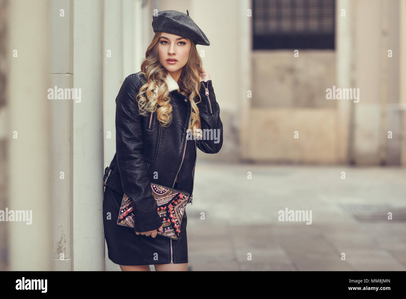 Bionda donna russa in background urbano. Bellissima fanciulla indossando beret, nero giacca di pelle e mini gonna in piedi in strada. Piuttosto femal Foto Stock